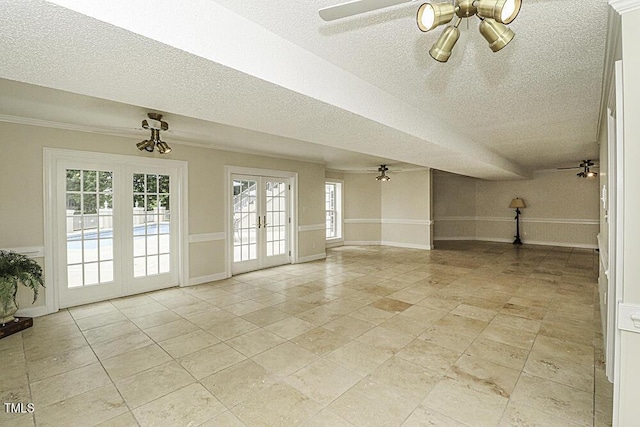 empty room with a wealth of natural light, a textured ceiling, ceiling fan, and french doors