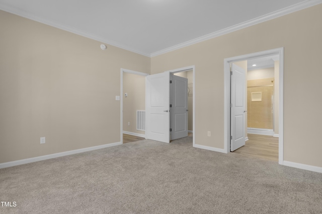 unfurnished bedroom with light carpet, a walk in closet, ornamental molding, and connected bathroom