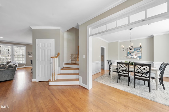 dining area featuring wainscoting, light wood-style flooring, stairway, an inviting chandelier, and crown molding