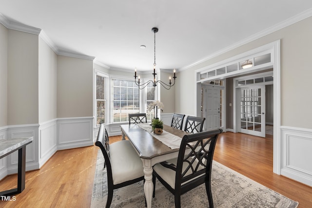 dining room with light wood-type flooring, a chandelier, crown molding, and wainscoting