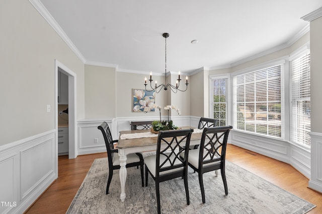 dining space featuring a notable chandelier, a decorative wall, ornamental molding, wainscoting, and wood finished floors