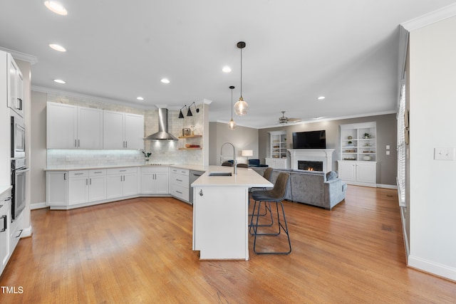 kitchen featuring appliances with stainless steel finishes, wall chimney range hood, a peninsula, a lit fireplace, and a kitchen breakfast bar