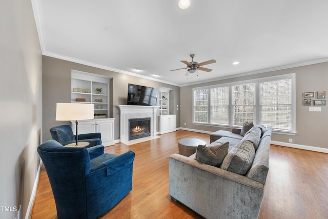 living area featuring a fireplace with flush hearth, ornamental molding, wood finished floors, and baseboards