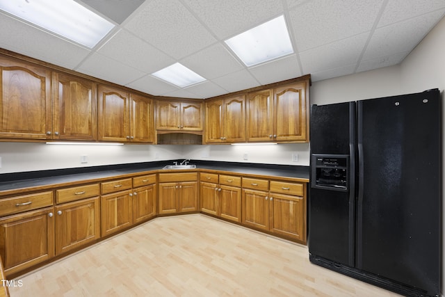 kitchen with dark countertops, light wood-type flooring, brown cabinetry, and black fridge