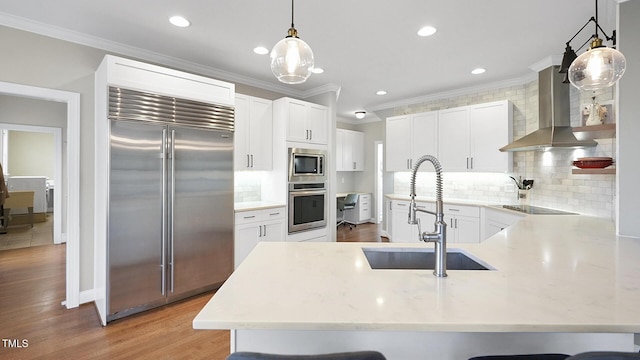 kitchen featuring ornamental molding, a sink, built in appliances, a peninsula, and wall chimney exhaust hood