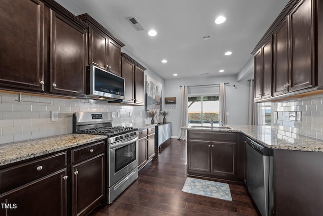 kitchen with sink, dark wood-type flooring, appliances with stainless steel finishes, dark brown cabinets, and light stone counters