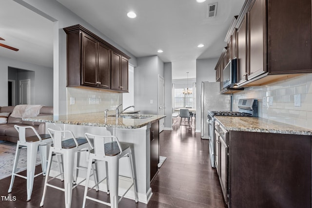 kitchen with sink, a breakfast bar, appliances with stainless steel finishes, light stone counters, and kitchen peninsula