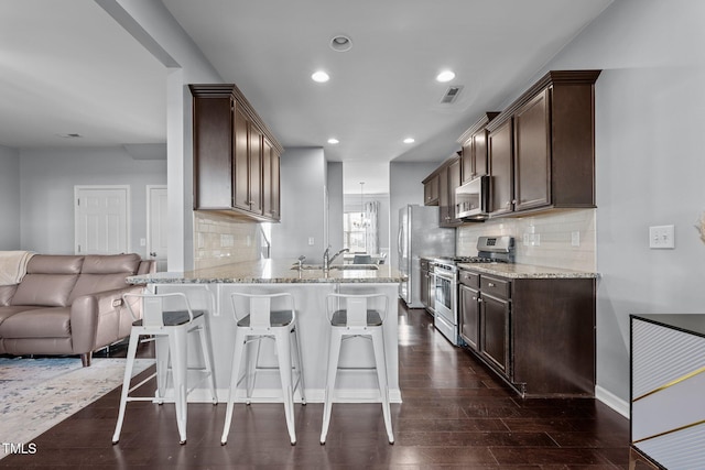 kitchen with a breakfast bar, dark hardwood / wood-style floors, decorative backsplash, light stone counters, and stainless steel appliances