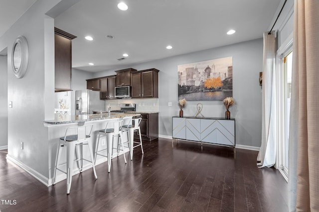 kitchen featuring a breakfast bar area, light stone counters, dark hardwood / wood-style floors, kitchen peninsula, and stainless steel appliances