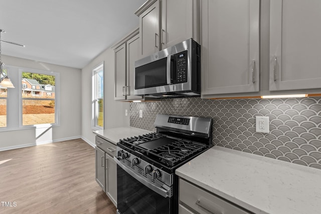 kitchen featuring gray cabinetry, stainless steel appliances, light stone countertops, light hardwood / wood-style floors, and decorative backsplash