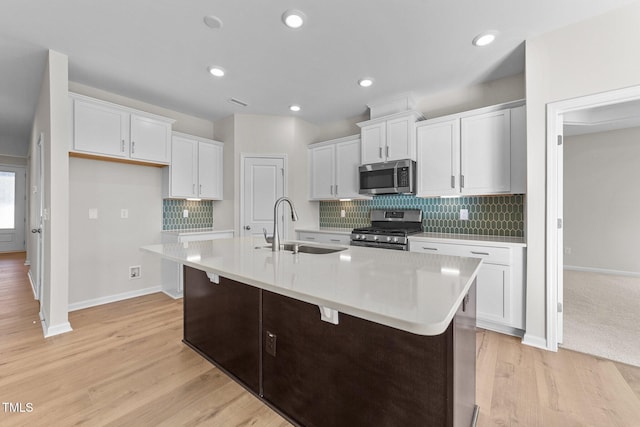 kitchen with appliances with stainless steel finishes, sink, a center island with sink, and white cabinets