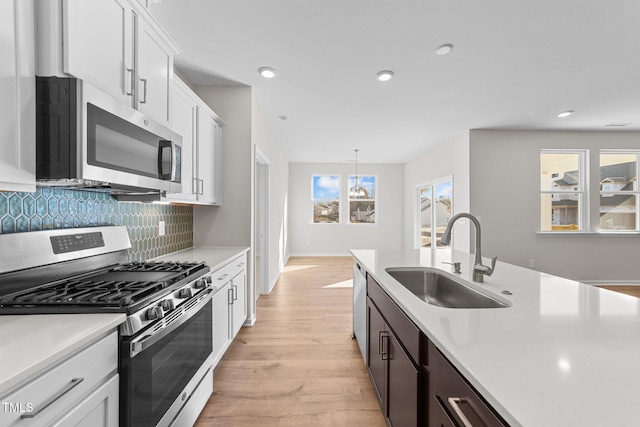 kitchen featuring white cabinetry, sink, backsplash, hanging light fixtures, and stainless steel appliances