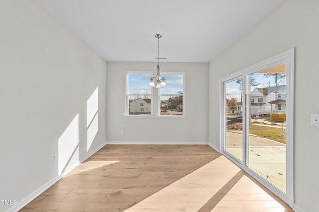 unfurnished dining area with a notable chandelier and light wood-type flooring