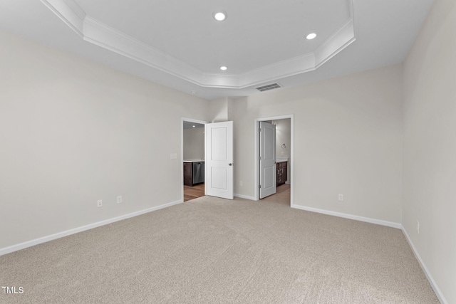 unfurnished bedroom featuring a tray ceiling, ornamental molding, light colored carpet, and ensuite bath