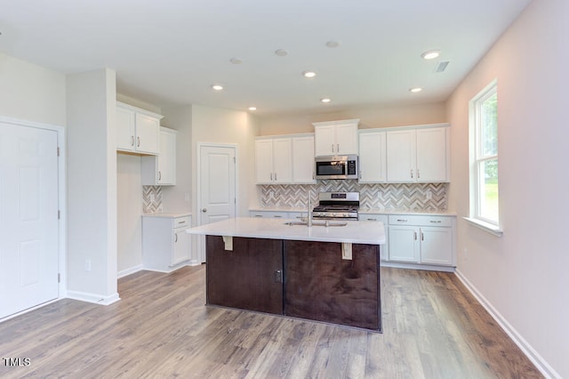 kitchen with sink, white cabinetry, stainless steel appliances, a center island with sink, and decorative backsplash