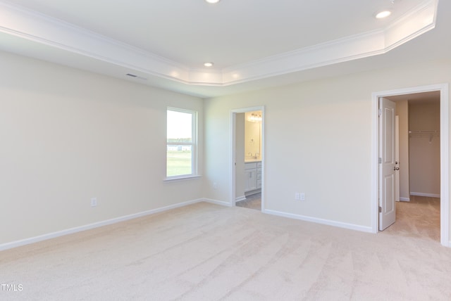 unfurnished bedroom featuring a raised ceiling, crown molding, a walk in closet, and light carpet