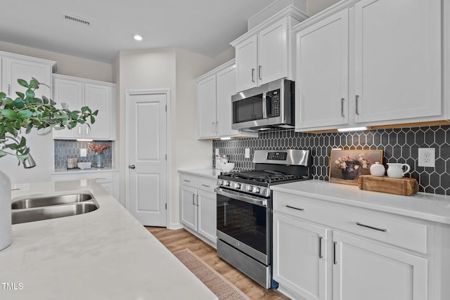 kitchen with stainless steel appliances, white cabinets, and light hardwood / wood-style flooring