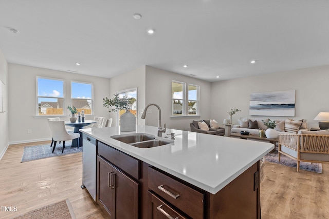 kitchen featuring stainless steel dishwasher, an island with sink, sink, and light wood-type flooring