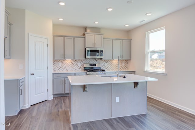 kitchen with stainless steel appliances, gray cabinets, a kitchen island with sink, and decorative backsplash