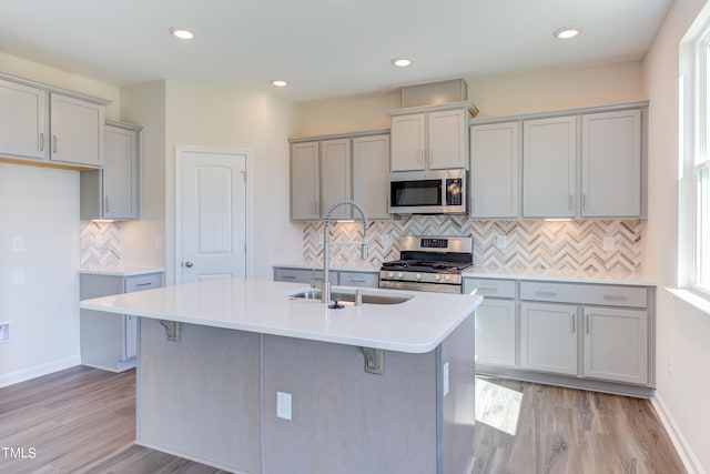 kitchen with stainless steel appliances, a kitchen island with sink, sink, and gray cabinetry