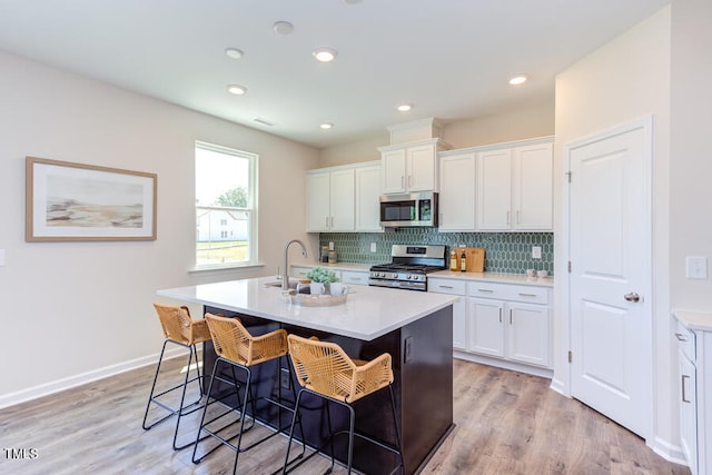 kitchen with appliances with stainless steel finishes, white cabinetry, decorative backsplash, a kitchen island with sink, and light hardwood / wood-style floors