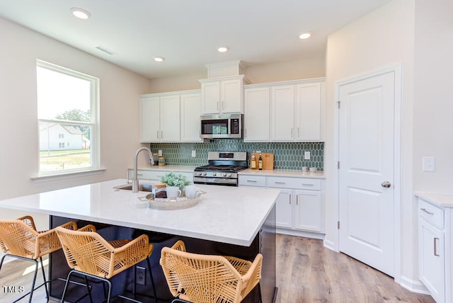 kitchen with appliances with stainless steel finishes, a kitchen island with sink, and white cabinets