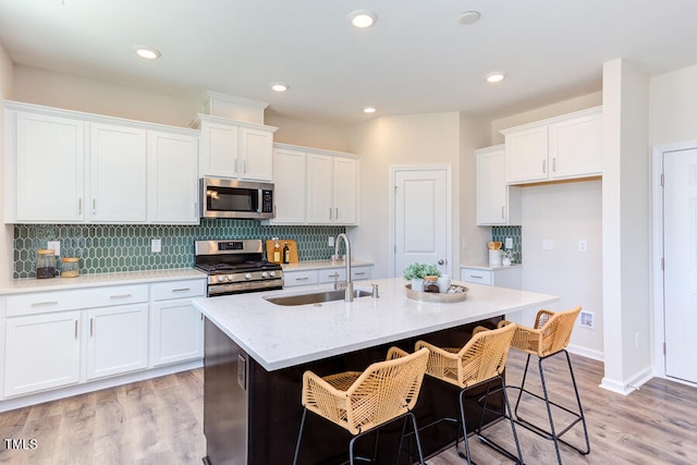 kitchen with stainless steel appliances, white cabinetry, sink, and a center island with sink