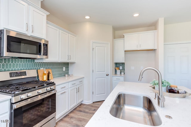 kitchen with sink, appliances with stainless steel finishes, light stone countertops, white cabinets, and decorative backsplash