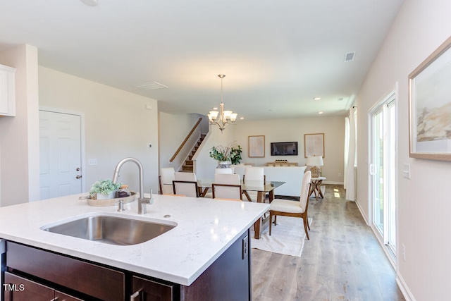 kitchen featuring sink, hanging light fixtures, dark brown cabinets, a center island with sink, and light wood-type flooring