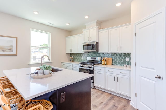 kitchen with stainless steel appliances, white cabinetry, a breakfast bar area, and an island with sink