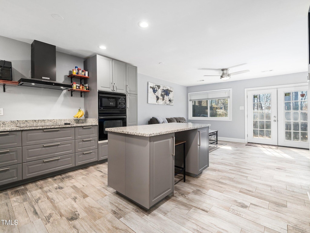 kitchen featuring wall chimney range hood, a breakfast bar, gray cabinetry, a center island, and black appliances