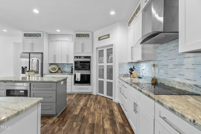 kitchen featuring wall chimney range hood, appliances with stainless steel finishes, white cabinetry, dark hardwood / wood-style floors, and light stone countertops