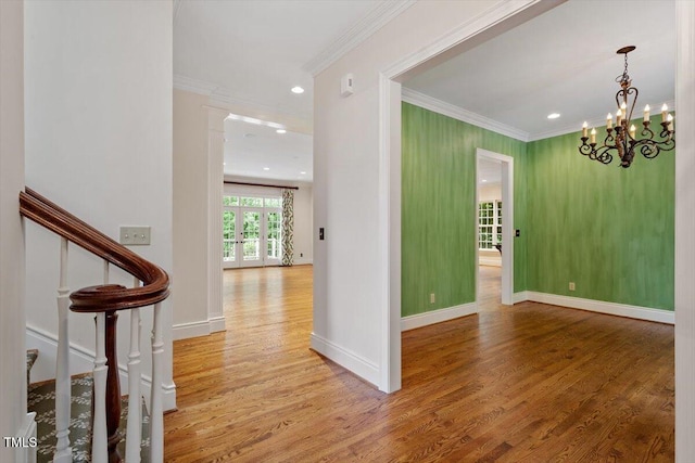corridor with crown molding, wood finished floors, stairway, a chandelier, and baseboards