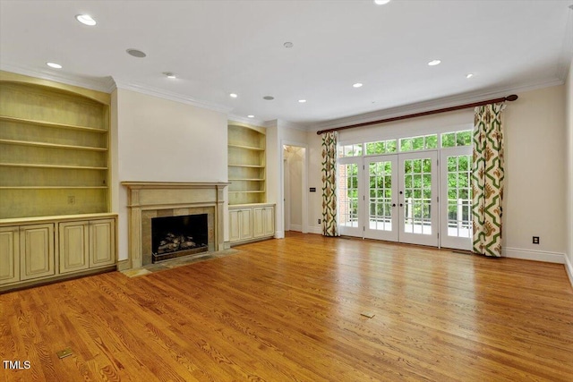 unfurnished living room with light wood finished floors, crown molding, a premium fireplace, baseboards, and built in features