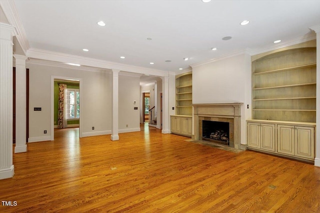 unfurnished living room with ornamental molding, light wood-style flooring, built in shelves, decorative columns, and a high end fireplace