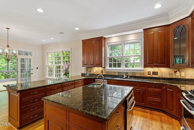 kitchen featuring a sink, a kitchen island with sink, stainless steel appliances, light wood-style flooring, and crown molding