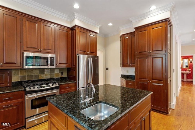 kitchen featuring stainless steel appliances, a sink, light wood finished floors, tasteful backsplash, and dark stone countertops