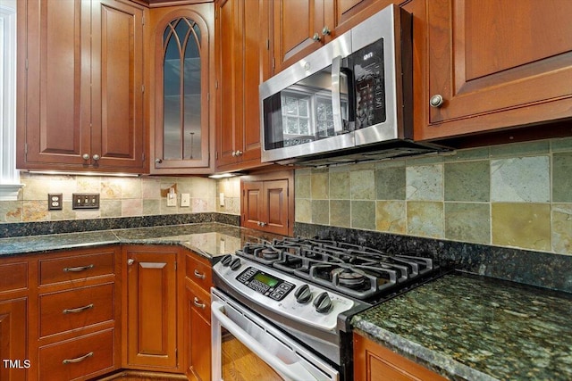 kitchen featuring appliances with stainless steel finishes, glass insert cabinets, brown cabinetry, and tasteful backsplash