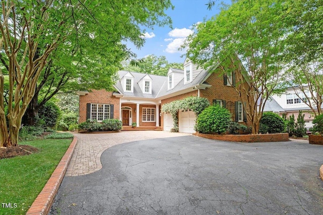 cape cod home with driveway, brick siding, a porch, and a garage