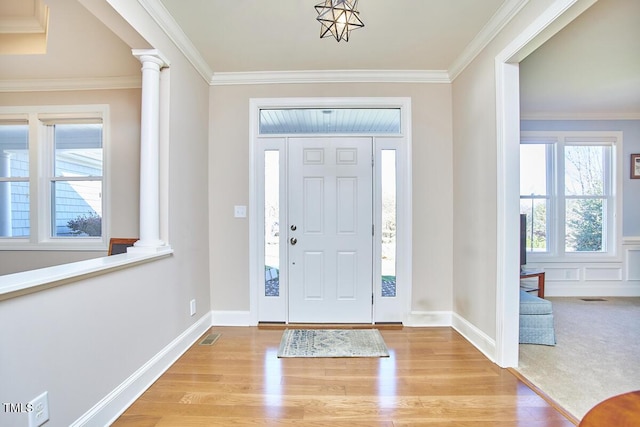 entryway with ornate columns, ornamental molding, and light wood-type flooring