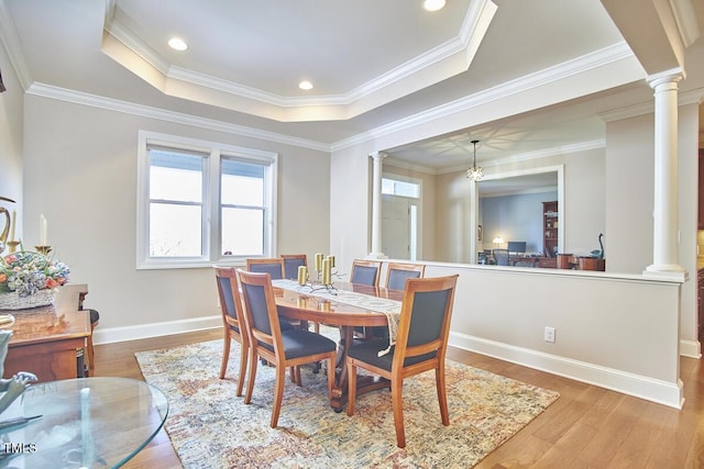 dining room with decorative columns, wood-type flooring, crown molding, and a tray ceiling