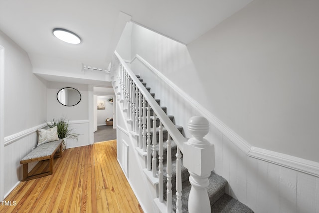 stairway featuring wood finished floors and a wainscoted wall