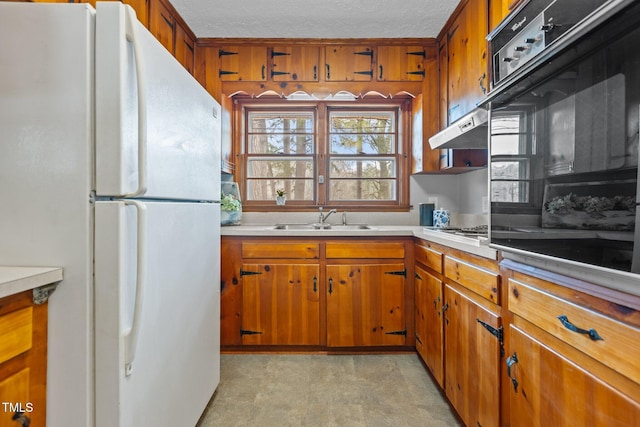 kitchen with sink, a textured ceiling, white refrigerator, stainless steel gas stovetop, and oven