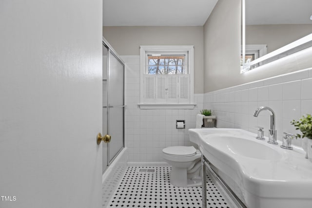 bathroom featuring enclosed tub / shower combo, toilet, tile patterned flooring, and tile walls