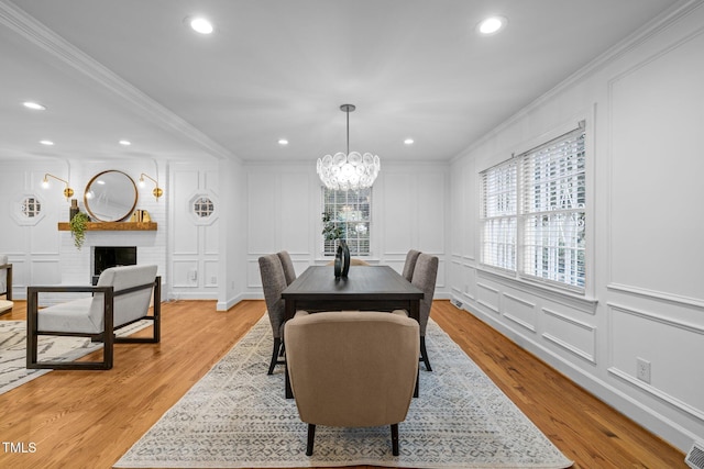 dining room featuring ornamental molding, a large fireplace, an inviting chandelier, and light hardwood / wood-style floors