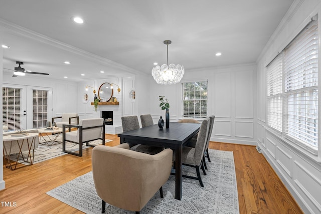 dining area featuring crown molding, a fireplace, ceiling fan with notable chandelier, and light wood-type flooring