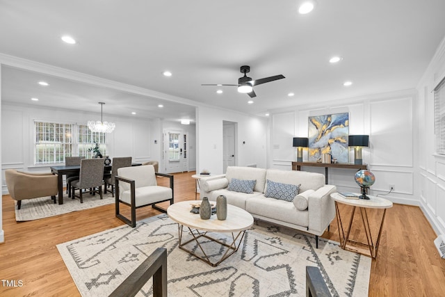 living room featuring ceiling fan with notable chandelier, ornamental molding, and light wood-type flooring