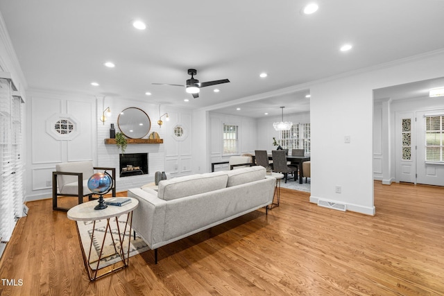 living room with ornamental molding, a brick fireplace, a healthy amount of sunlight, and light hardwood / wood-style floors