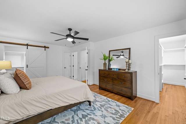 bedroom featuring ceiling fan, a barn door, and light wood-type flooring