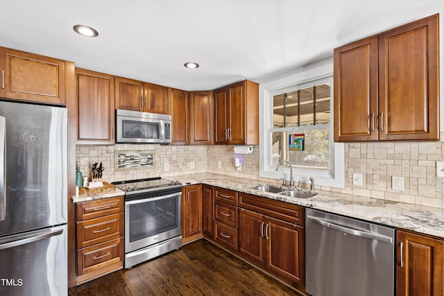 kitchen featuring appliances with stainless steel finishes, sink, dark hardwood / wood-style flooring, decorative backsplash, and light stone counters